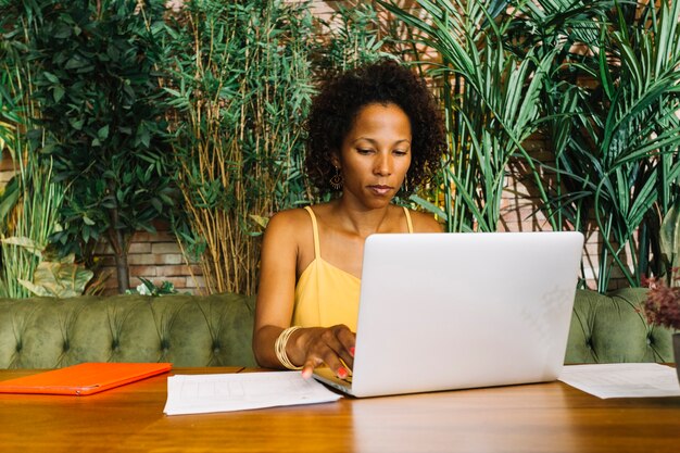 Mujer joven afroamericana sentada frente a plantas usando laptop