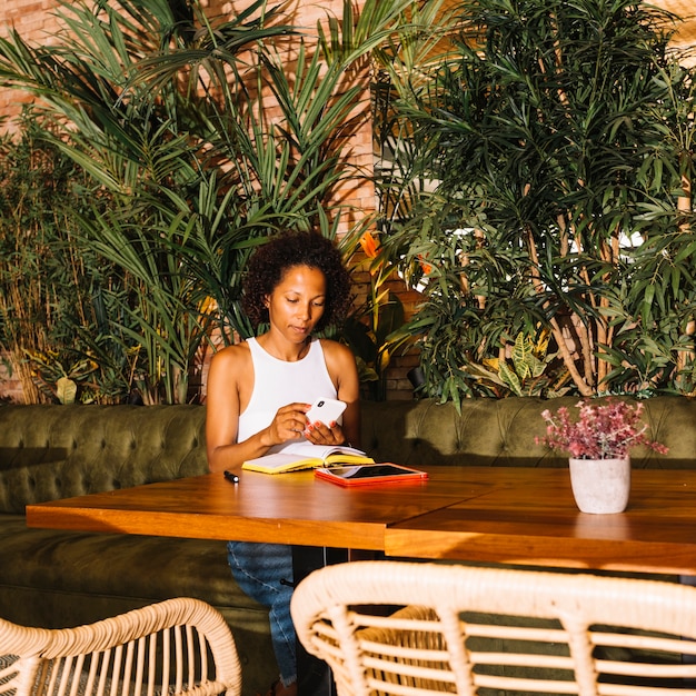 Mujer joven afroamericana usando teléfono inteligente en restaurante de lujo