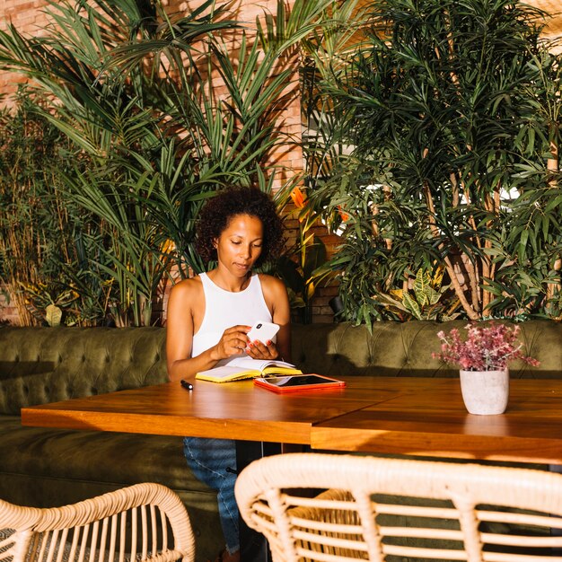 Mujer joven afroamericana usando teléfono inteligente en restaurante de lujo