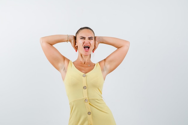 Foto gratuita mujer joven agarrando la cabeza con las manos mientras grita en vestido amarillo y parece agresivo