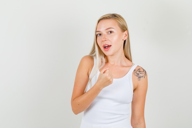 Mujer joven agarrando su mano en puño en camiseta blanca y mirando feliz