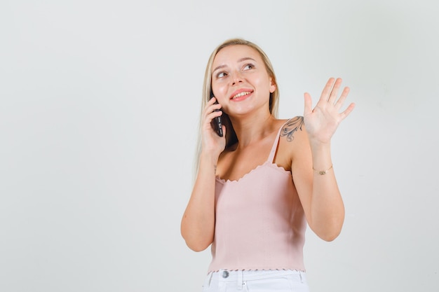 Mujer joven agitando la mano mientras habla por teléfono inteligente en camiseta