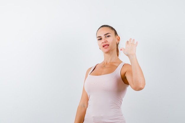 Foto gratuita mujer joven agitando la mano para saludar en camiseta blanca y mirando feliz, vista frontal.