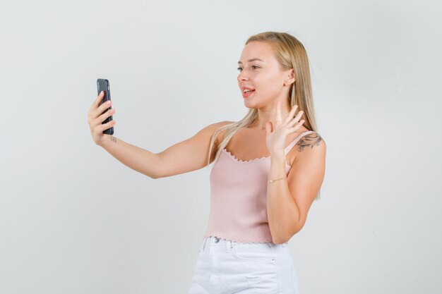 Mujer joven agitando la mano en videollamada en camiseta