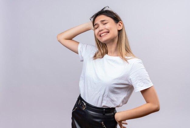 Una mujer joven agresiva en camiseta blanca con gafas de sol en la cabeza expresando negatividad mientras mantiene la mano en la cabeza