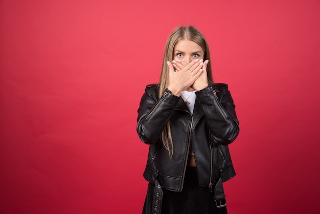Mujer joven aislada en la pared roja conmocionada cubriendo la boca con las manos
