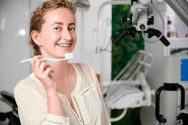 Mujer joven alegre con aparatos ortopédicos en los dientes con cepillo de dientes
