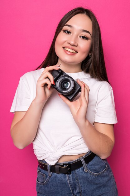 Mujer joven alegre con cámara de fotos en pared rosa