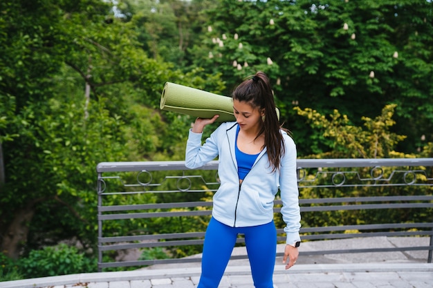 Mujer joven alegre deportes caminando en parque urbano con alfombra de fitness.