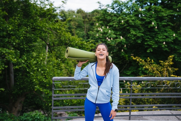 Mujer joven alegre deportes caminando en parque urbano con alfombra de fitness.