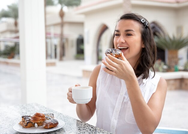 Mujer joven alegre disfrutando de un café por la mañana con donas en la terraza al aire libre