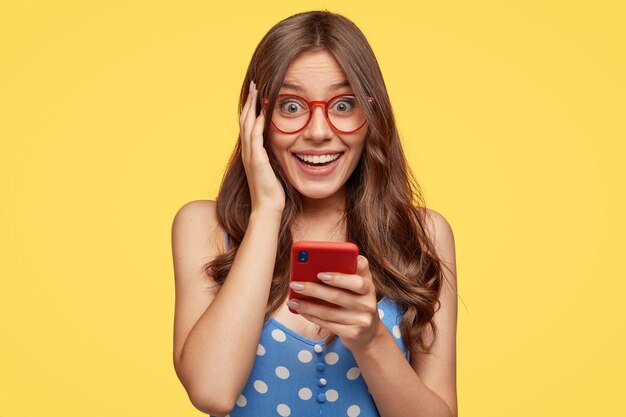 Mujer joven alegre con gafas posando contra la pared amarilla