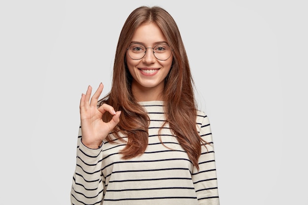 Mujer joven alegre con gafas posando contra la pared blanca