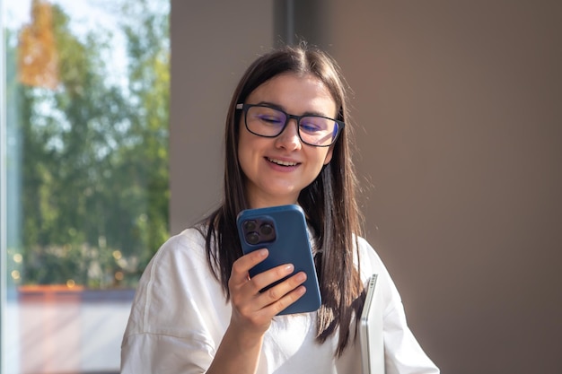 Mujer joven alegre en gafas con un teléfono inteligente en sus manos