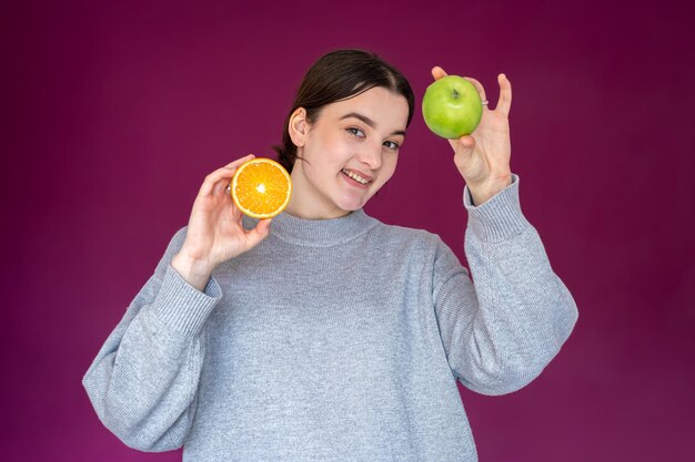 Mujer joven alegre con manzana y naranja sobre fondo púrpura