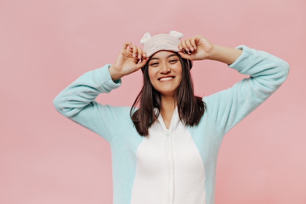 Foto gratuita mujer joven alegre en pijama de menta sonríe sinceramente, mira al frente y se pone la máscara para dormir