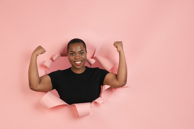 Foto gratuita mujer joven alegre posa en pared de agujero de papel de coral rasgado emocional y expresiva