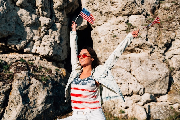 Foto gratuita mujer joven alegre que agita banderas americanas en rocas