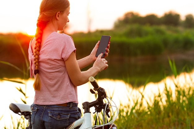 Mujer joven alegre que monta una bicicleta en el paseo de la ribera y del prado.