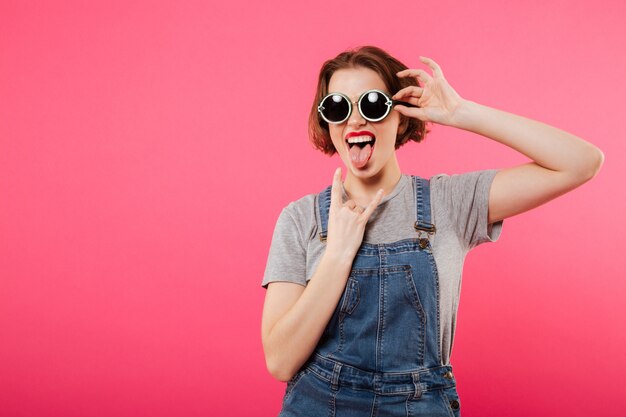 Mujer joven alegre que muestra gesto de la lengua y de la roca.