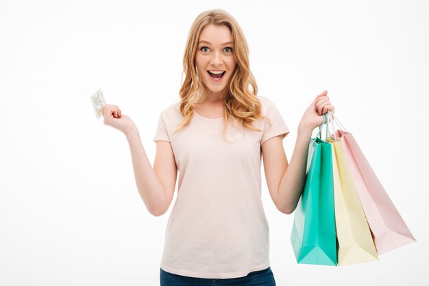 Mujer joven alegre que sostiene la tarjeta de crédito y bolsos de compras.