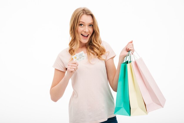 Mujer joven alegre que sostiene la tarjeta de crédito y bolsos de compras.