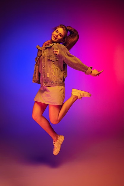 Mujer joven alegre saltando posando aislada sobre fondo rosa azul degradado en luz de neón