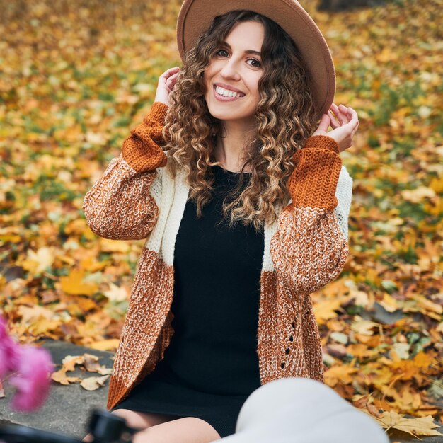 Mujer joven alegre sentada en la calle de otoño