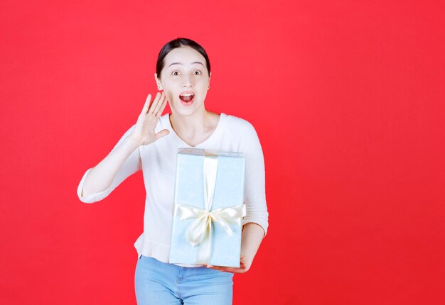 Mujer joven alegre sosteniendo caja de regalo y diciendo algo