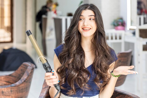 Mujer joven alegre sosteniendo secador de pelo y sonriendo en la barbería Foto de alta calidad