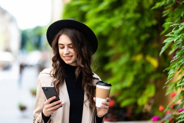 Mujer joven alegre con taza de papel teléfono de surf en la calle