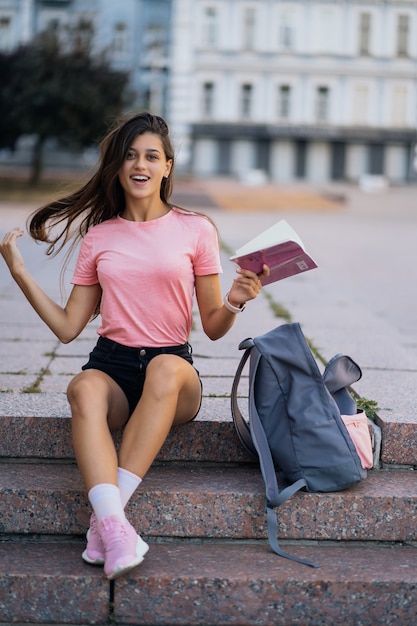 Mujer joven alegre tomando notas mientras está sentado en los pasos otdoors