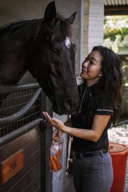 Una mujer joven alimenta a un caballo con zanahorias.