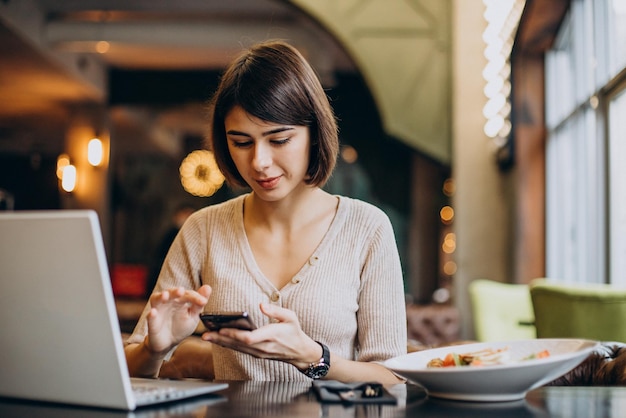 Mujer joven almorzando en un café y trabajando en una laptop