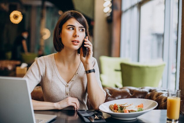 Mujer joven almorzando en un café y trabajando en una laptop