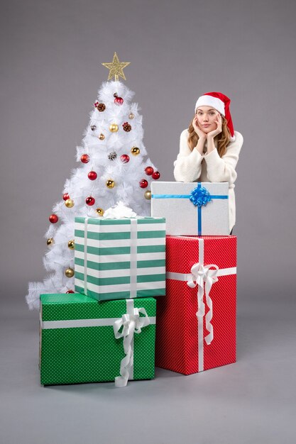 mujer joven alrededor de regalos de navidad en gris