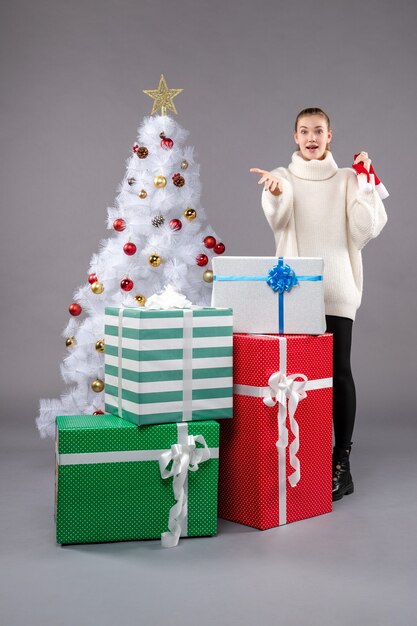 mujer joven alrededor de regalos de navidad en gris