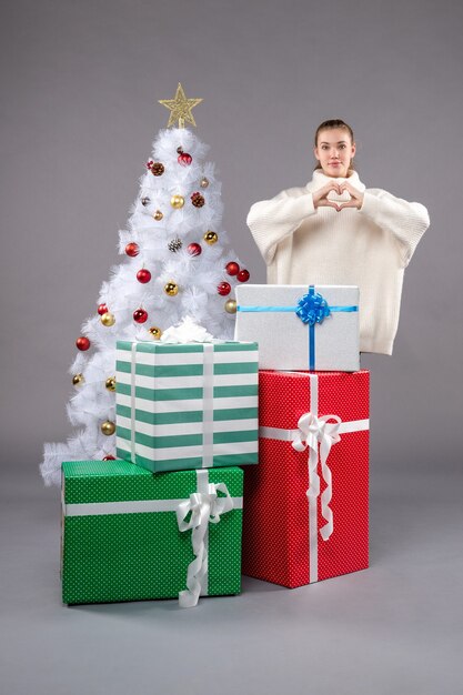 mujer joven alrededor de regalos de navidad en gris