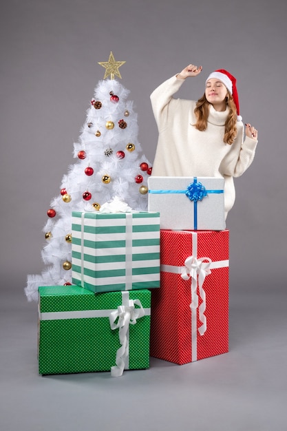 mujer joven alrededor de regalos de navidad en gris