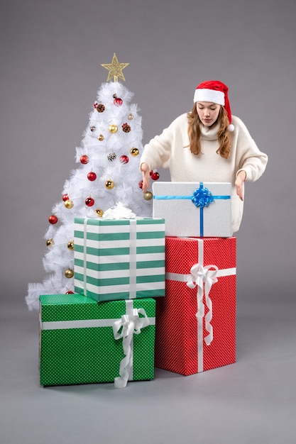 mujer joven alrededor de regalos de navidad en gris
