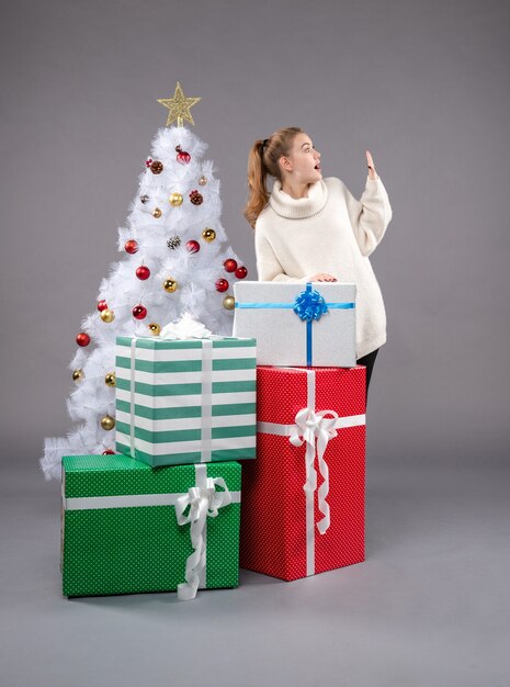 mujer joven alrededor de regalos de navidad en gris