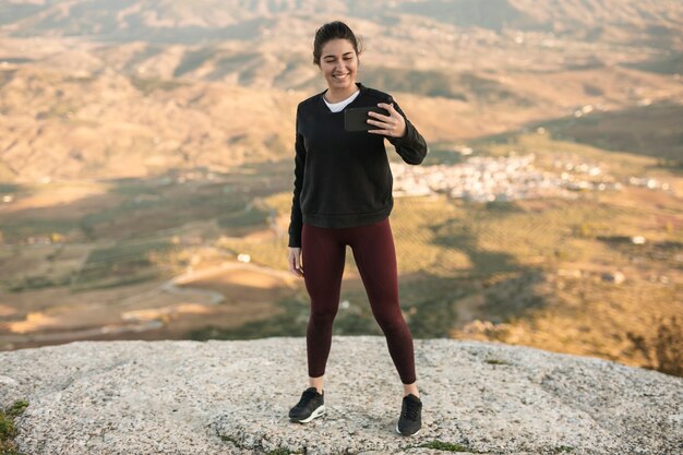 Mujer joven de alto ángulo en montaña tomando selfie