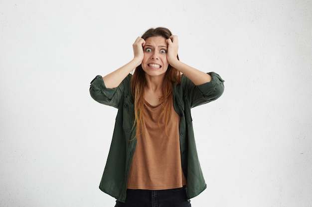 Foto gratuita mujer joven ansiosa y vestida informalmente, estresada que se arranca el cabello sintiendo tensión y estrés mientras enfrenta problemas, no puede soportar la presión, apretar los dientes y mantener los ojos abiertos.