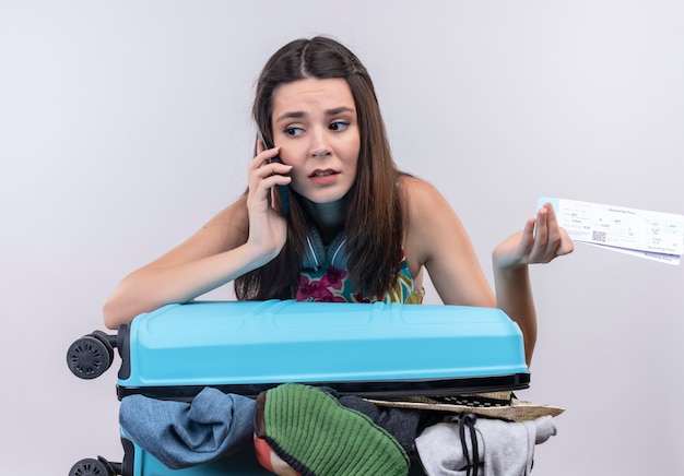 Mujer joven ansioso viajero hablando por teléfono sosteniendo boletos en pared blanca aislada