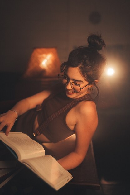 Mujer joven con anteojos leyendo un libro en una acogedora sala de estar