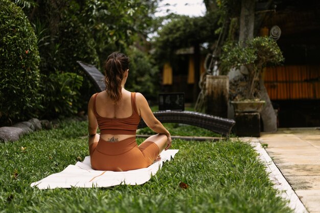 Mujer joven con apariencia corporal positiva practicando yoga sola en la terraza junto a la piscina en la isla tropical de Bali, Indonesia. Deporte, fitness, concepto de estilo de vida saludable.