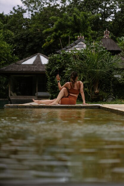 Mujer joven con apariencia corporal positiva practicando yoga sola en la terraza junto a la piscina en la isla tropical de Bali, Indonesia. Deporte, fitness, concepto de estilo de vida saludable.