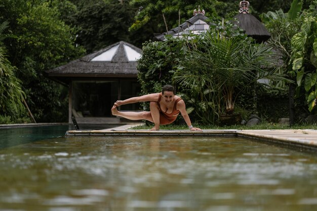 Mujer joven con apariencia corporal positiva practicando yoga sola en la terraza junto a la piscina en la isla tropical de Bali, Indonesia. Deporte, fitness, concepto de estilo de vida saludable.
