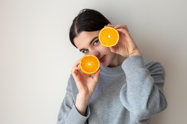 Una mujer joven con apetitosas mitades de una naranja sobre un fondo blanco.