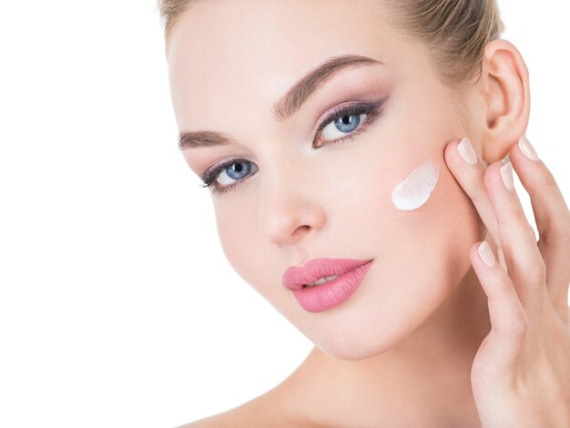 Mujer joven aplica crema cosmética en la cara.